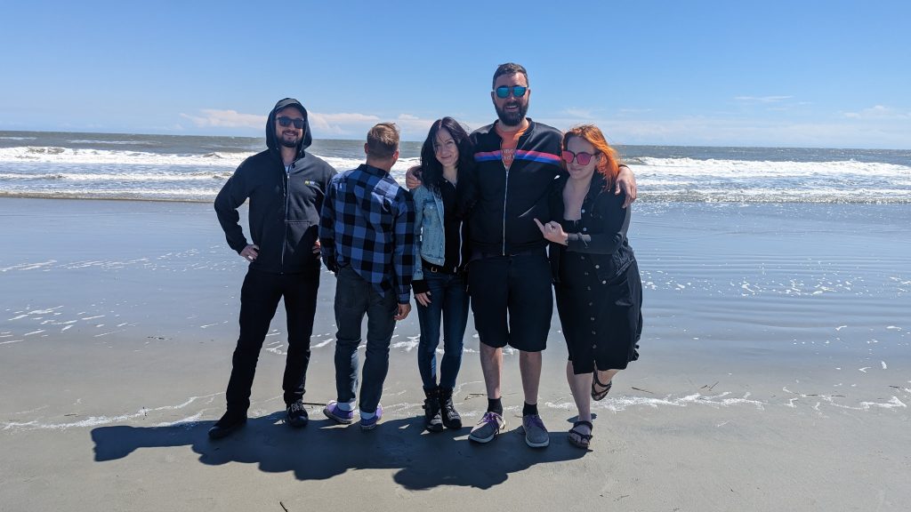 The Cancellations pose for a group photo on the beach in Charleston. Ellie is flipping off Dan, who is facing backwards.