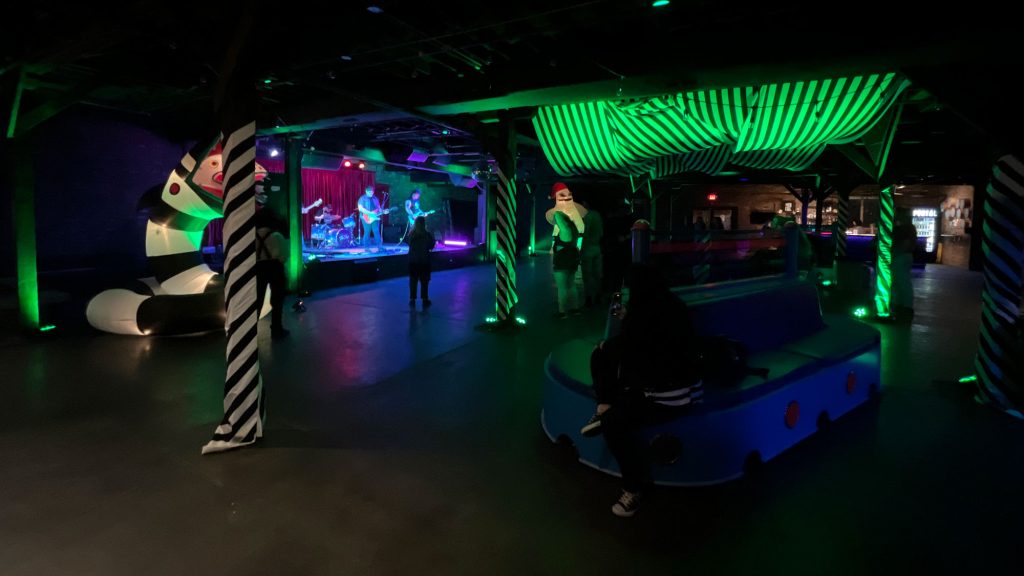 Tim Burton inspired decor around the venue in Louisville. A band is on stage getting ready to play and a photographer takes their picture. There is a giant blow up sand snake, and black and white striped cloth hangs over the dance floor.
