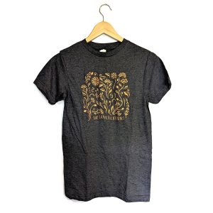 The Cancellations "Garden Secrets" tee with a swirly, flowery design in shimmery orange ink on a heather black t-shirt.