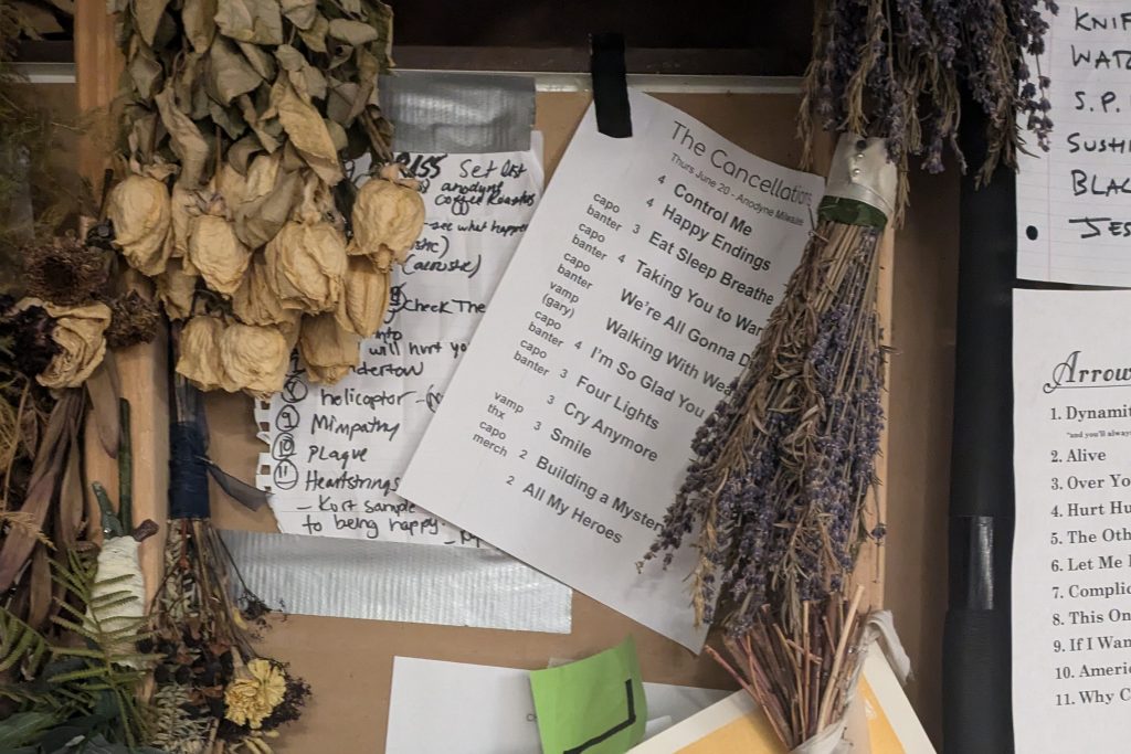 The green room wall at Anyodyne in Milwaukee. Hundreds of artists have taped up their set lists after their show, and their are dried flowers and show posters hanging around them. It is a really pretty arrangement in muted, earthy colors that celebrates all the music that has passed through the venue.