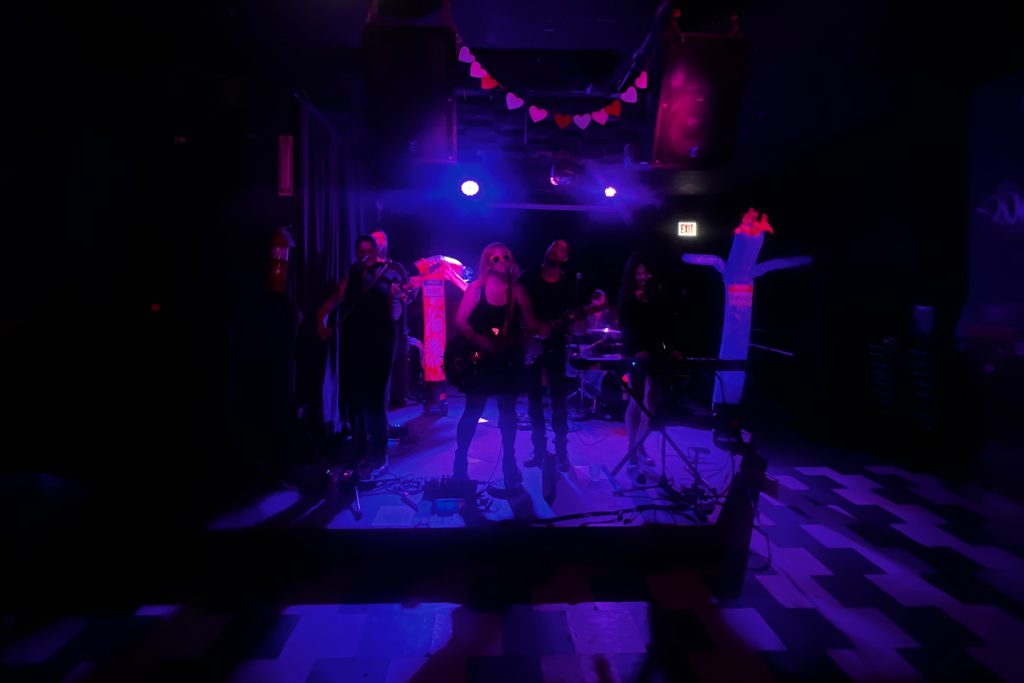 The Cancellations play on a dark stage in Chicago. Depression and Dance are flopping around. The photo is a little blurry in the darkness. The floor is a checkerboard and it it has an ominous vibe to it.